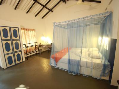 Helles Hotelzimmer mit Himmelbett, blauem Moskitonetz, Kleiderschrank und Schreibtisch