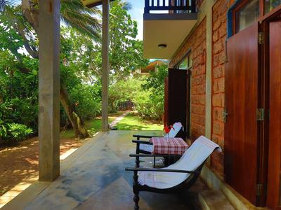 Einladende Terrasse mit Holzstuhl, buntem Kissen, Steinboden und grüner Gartenlandschaft.