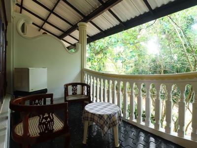 Überdachter Balkon mit Holzmöbeln, weißen Balustraden und Blick ins grüne Laub.