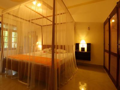 Gemütliches Schlafzimmer mit Himmelbett, transparentem Vorhang und warmem Gelblicht.