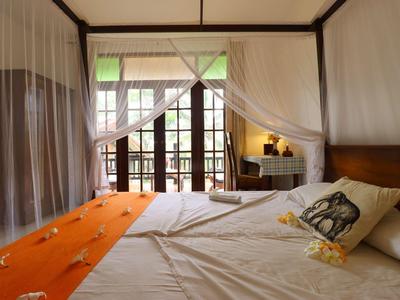 Gemütliches Schlafzimmer mit Doppelbett, weißem Moskitonetz, orangenem Teppich und Holzbalken.