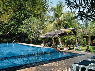 Ein ruhiger Poolbereich umgeben von Palmen und Liegestühlen in einer tropischen Hotelanlage.