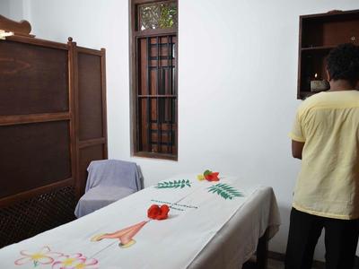 Zimmer mit Massageliege, dekoriert mit Blumen, und einer Person, die vor einem Regal steht.