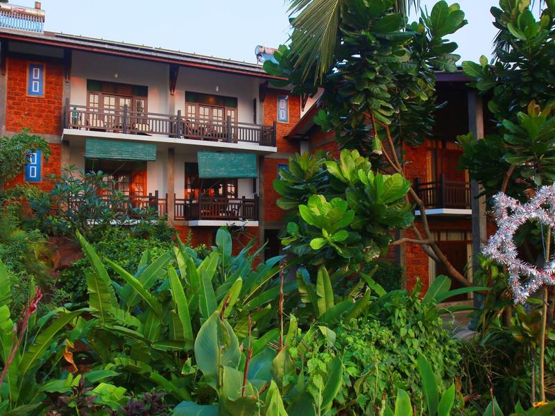 Mehrstöckiges Holzhaus in grünem Garten mit üppigen Pflanzen und Stern-Dekoration aus Ästen.