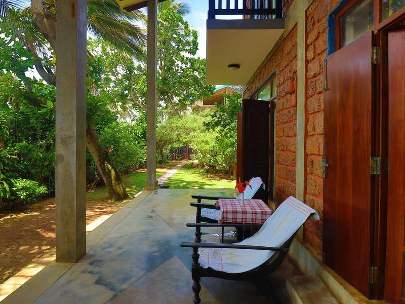 Einladende Terrasse mit Holzstuhl, buntem Kissen, Steinboden und grüner Gartenlandschaft.
