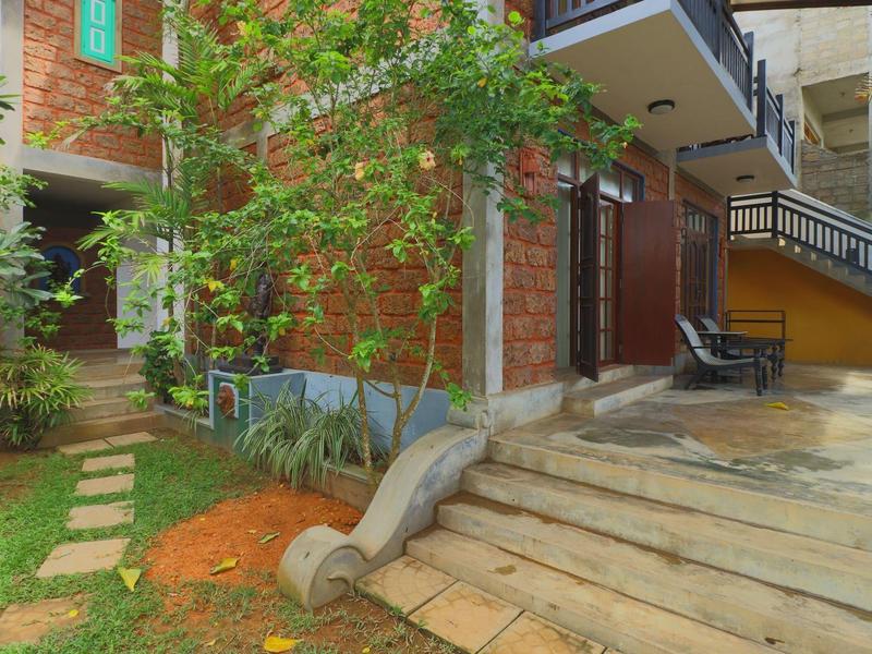 Haus mit roter Ziegelwand, Treppe, Pflasterweg und grünem Garten mit Bäumen und Pflanzen.