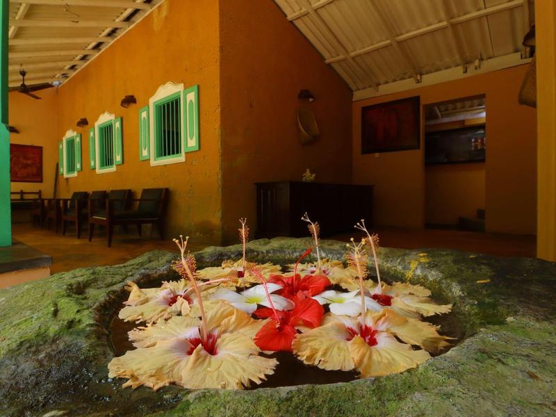 Innenhof mit Steinbecken, darin schwimmende bunte Blüten, umgeben von orangefarbenen Wänden.
