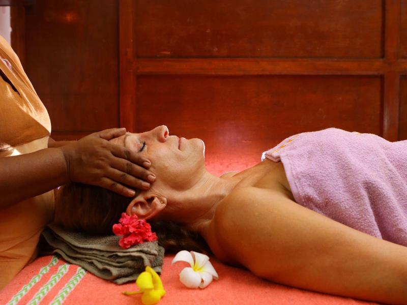 Frau liegt entspannt mit rosa Handtuch, während Hände ihren Kopf sanft massieren.