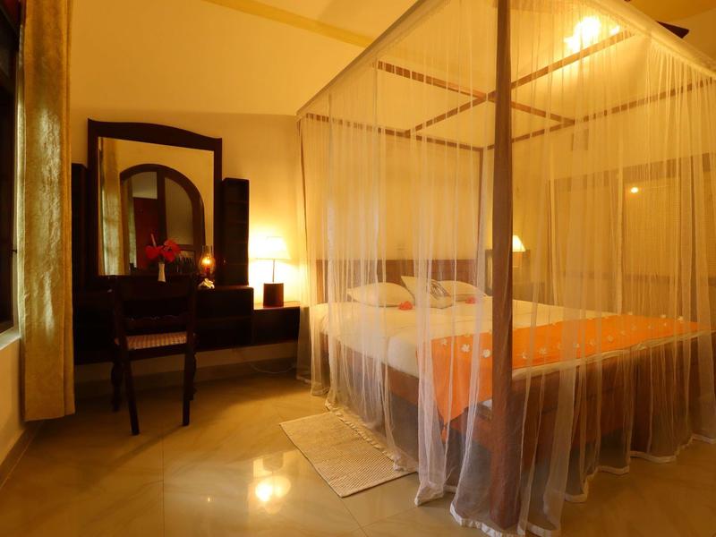 Gemütliches Schlafzimmer mit Himmelbett, Moskitonetz und Holzmöbeln in warmem Licht.