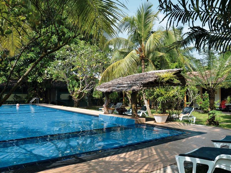 Ein ruhiger Poolbereich umgeben von Palmen und Liegestühlen in einer tropischen Hotelanlage.