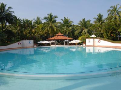 Large swimming pool with clear water, surrounded by palm trees and sun umbrellas.
