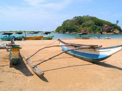 Tradiční rybářská loď s výložníky na písčité pláži před malým ostrovem.