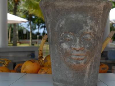 Stone planter with face design in front of tropical background.