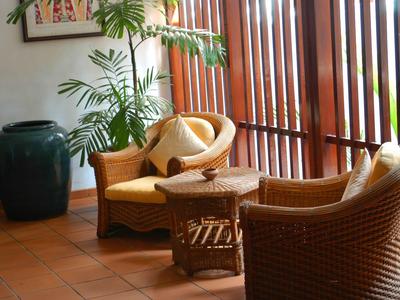 Cozy seating area with rattan chairs, cushions, table, and plants in front of wooden blinds.