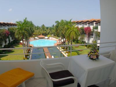 View from a terrace with table and chairs overlooking a pool and palm trees at a hotel resort.