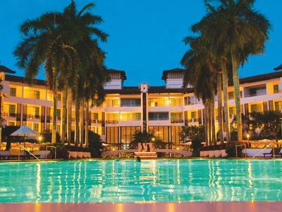 Lit hotel with pool and palm trees at dusk.