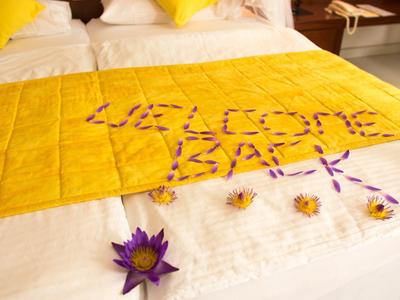 A yellow cloth on the bed with 'WELCOME BACK' spelled in petals, surrounded by flowers.
