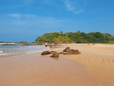 A quiet sandy beach with rocks and a wooded peninsula in the background under a blue sky.
