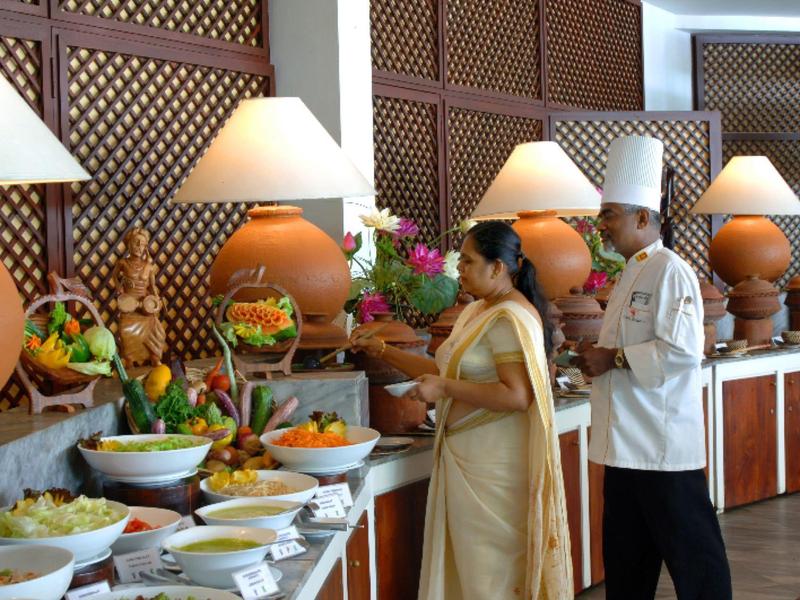Buffet area with fruits and salads, a woman in traditional attire and a chef stand side by side.