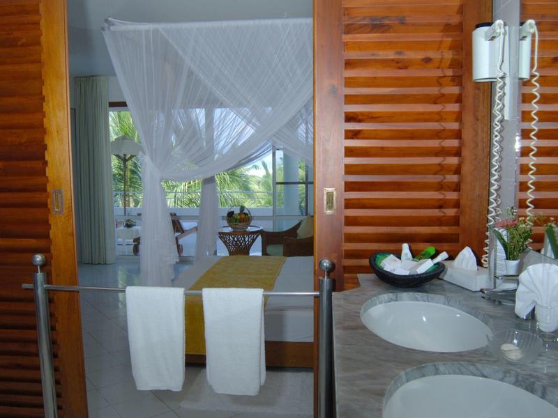 A bathroom with two sinks and a view into a bedroom with a mosquito net over the window.
