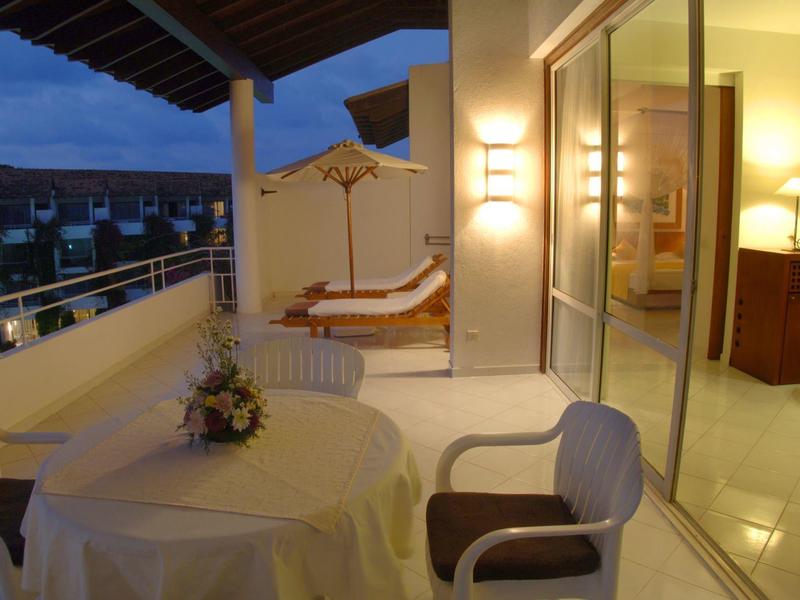 Lit balcony with table, chairs, and lounge chairs at dusk in a hotel.