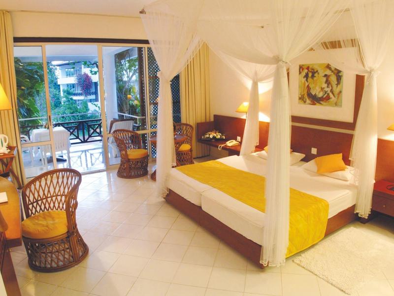 Bright hotel room with canopy bed and view of balcony overlooking garden.