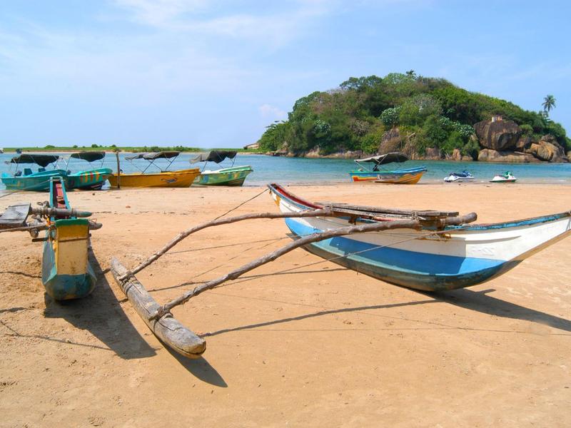 A traditional boat rests on a sandy beach with a wooded island in the background.