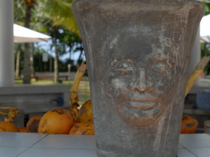 Stone planter with face design in front of tropical background.