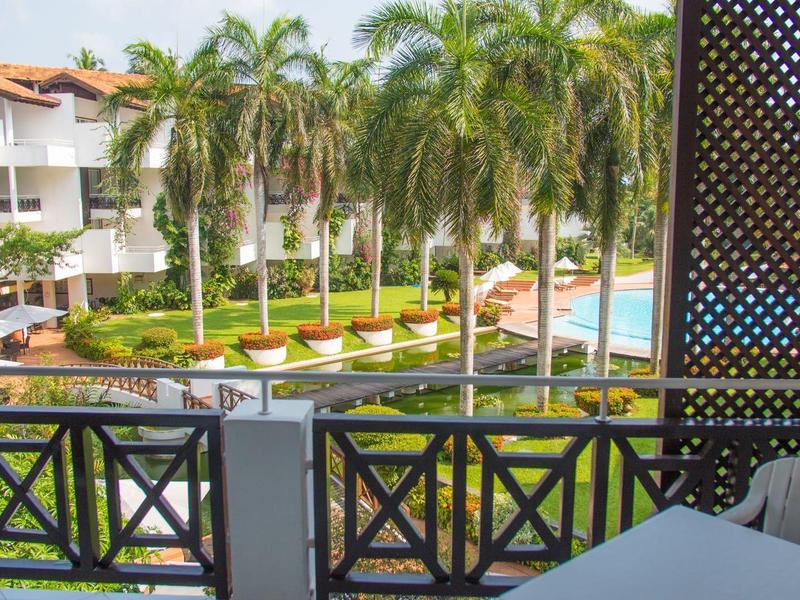 View from a hotel balcony overlooking a pool area with palm trees and white buildings.