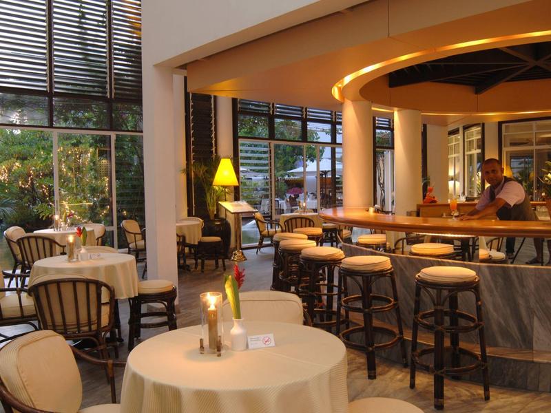 Bright restaurant with round tables, chairs, and a bar with stools.