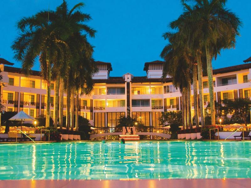 Lit hotel with pool and palm trees at dusk.