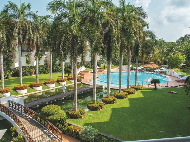 Hotel complex with pool, palm trees, and manicured garden under sunshine