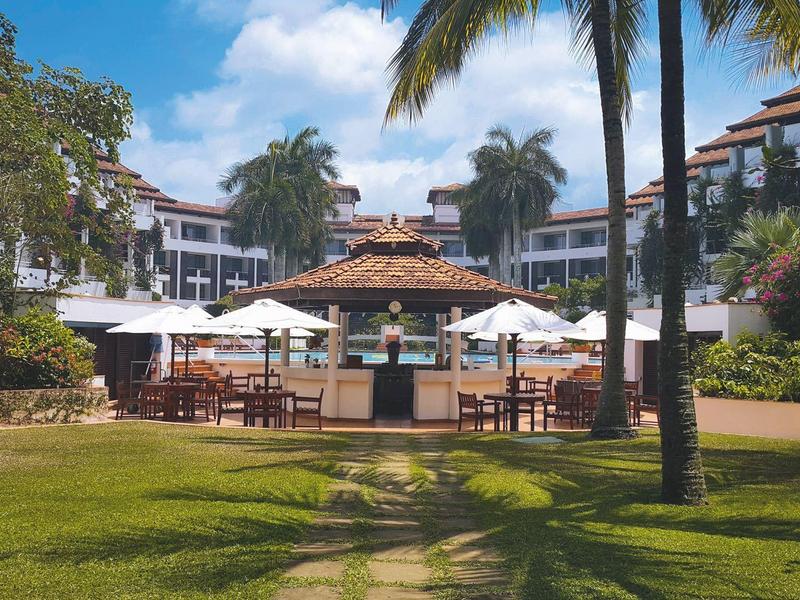 Sunny hotel garden with bar area, seating, and palm trees