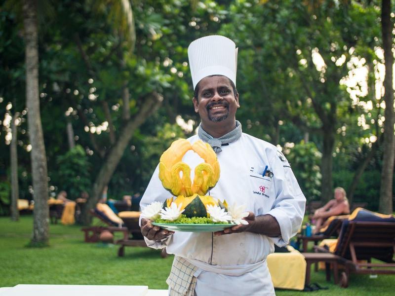 Smiling chef in white uniform holding plate with fruity dessert in garden