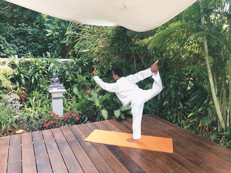 Person practicing yoga on a wooden platform in a lush garden setting