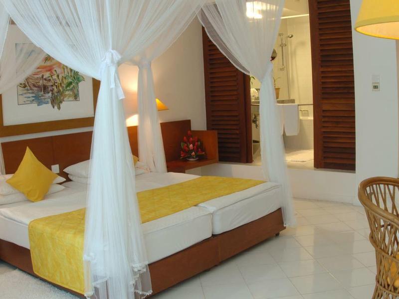 Bright hotel room with canopy bed, yellow accents, and wooden furniture.