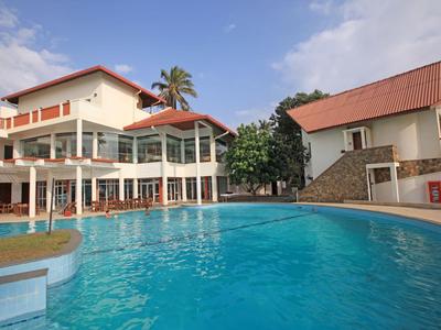 Großer Außenpool vor einem Hotelgebäude mit roten Dächern und Palmen.