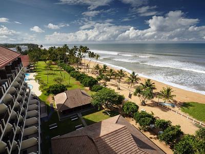 Výhled z hotelu na tropickou pláž s palmami a zataženou oblohou.