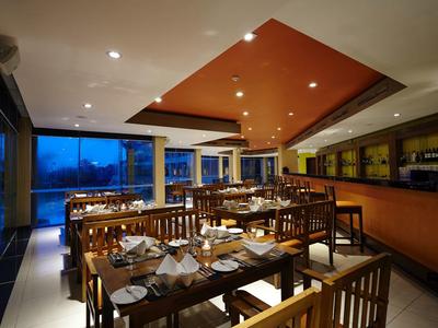 Moderní restaurace s dřevěným nábytkem a velkou skleněnou stěnou, večerní hotelová atmosféra.