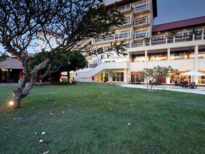 Velká tráva s stromem před osvětlenou budovou hotelu za soumraku.