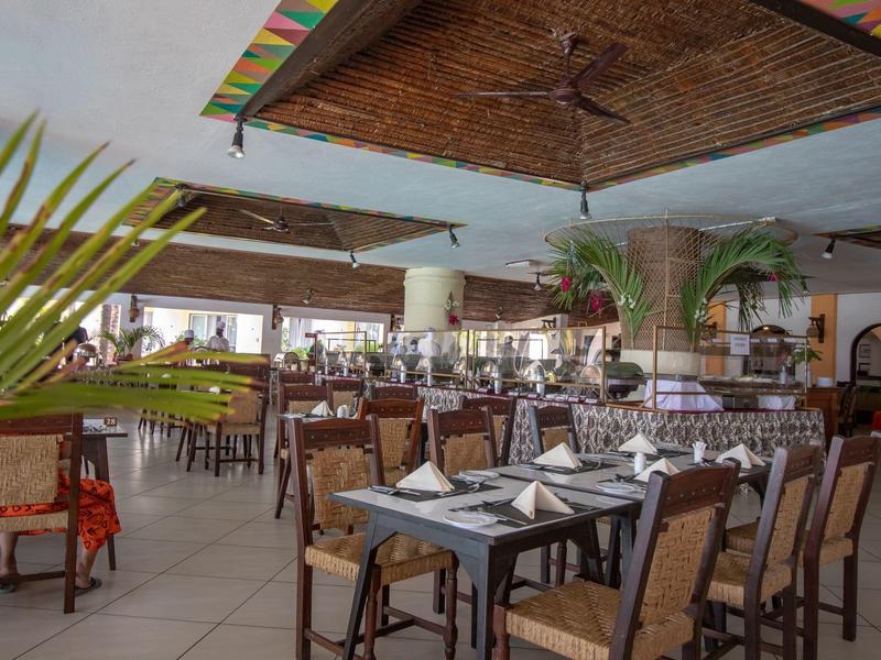 Elegantní restaurace s prostřenými stoly, proutěnými židlemi a tropickou výzdobou.