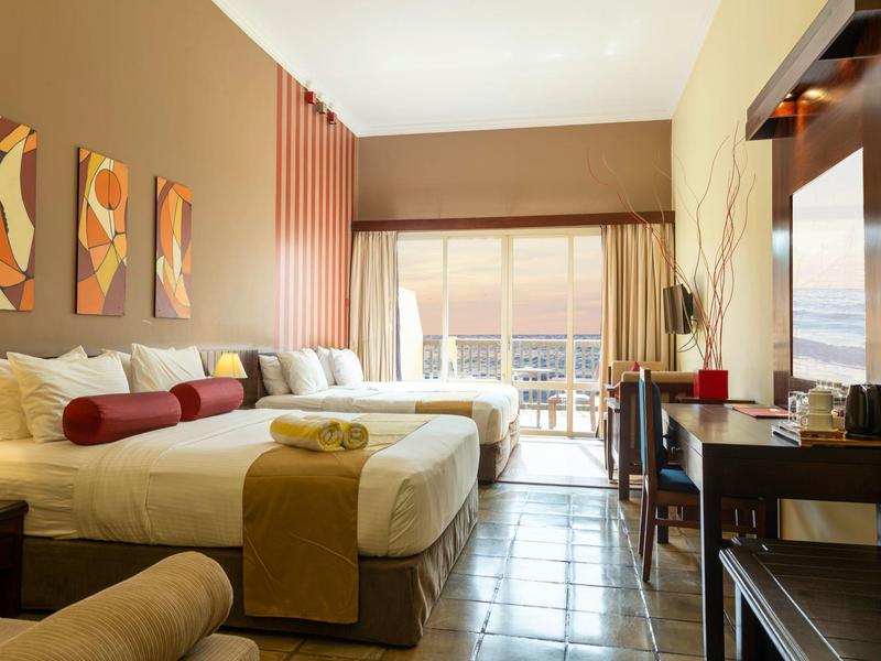 Světý hotelový pokoj se dvěma velkými postelemi, květinovou výzdobou a balkonem s výhledem.