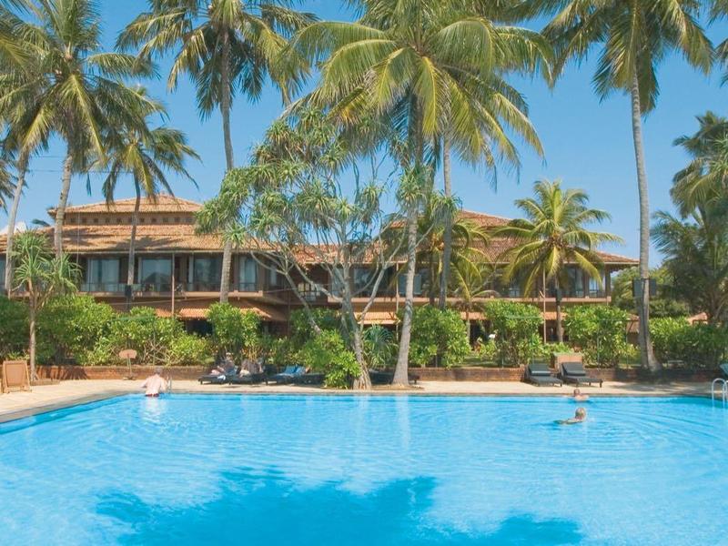 Groot zwembad omgeven door palmbomen en een hotelgebouw op de achtergrond bij zonnige lucht.