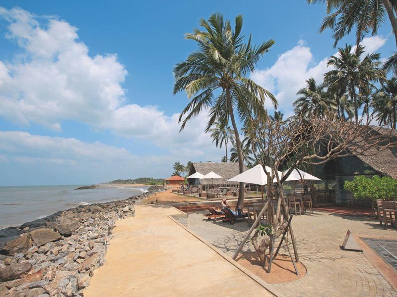 Strandpromenade met palmbomen en zitgedeeltes aan zee onder een blauwe lucht