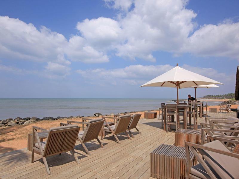 Houten terras met ligstoelen en tafels op het strand onder bewolkte lucht