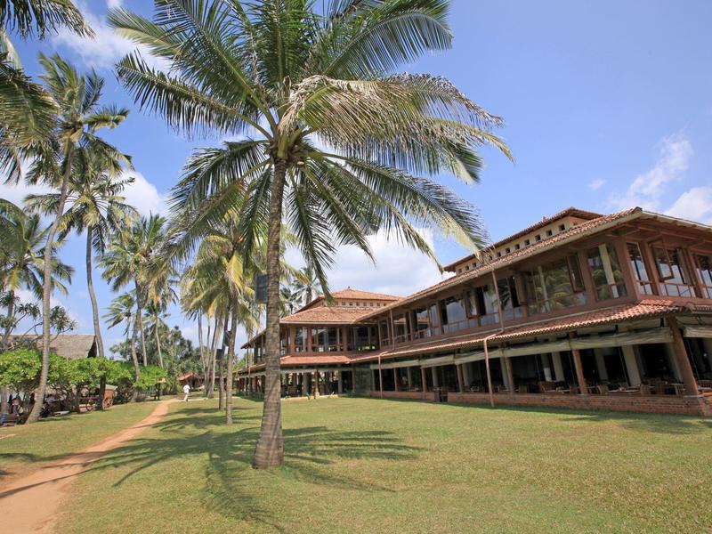 Groot resort met palmbomen en een tweeverdiepingen tellend gebouw onder een zonnige hemel.