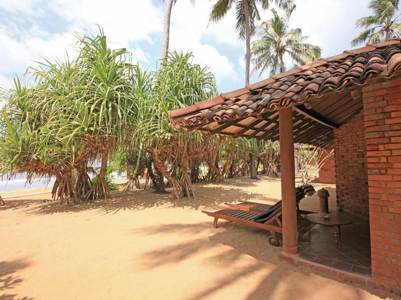 Strandhotel met bakstenen muren, beboste omgeving en palmbomen onder een zonnige hemel