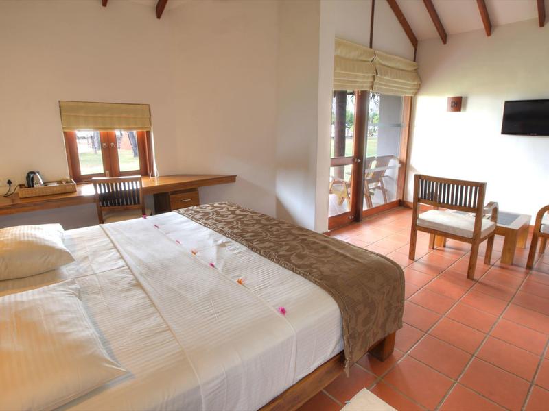 Licht ingericht hotelkamer met tweepersoonsbed, zithoek en terrasdeur met uitzicht naar buiten.