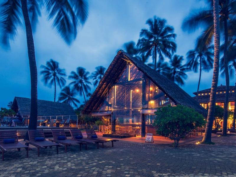 Strandresort met verlicht houten huis en palmbomen in de schemering.