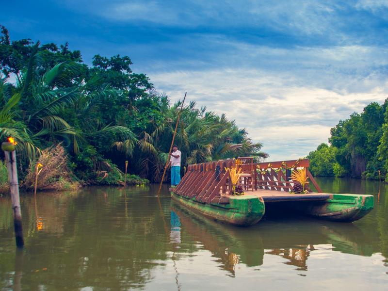 Rivier met groene veerboot en weelderige tropische begroeiing onder bewolkte lucht.